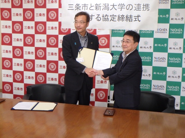 握手を交わす国定三条市長(左)と髙橋学長(右)