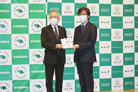 堂前洋一郎新潟県医師会長(左)と染矢俊幸医学部長(右)目録を掲げて記念撮影